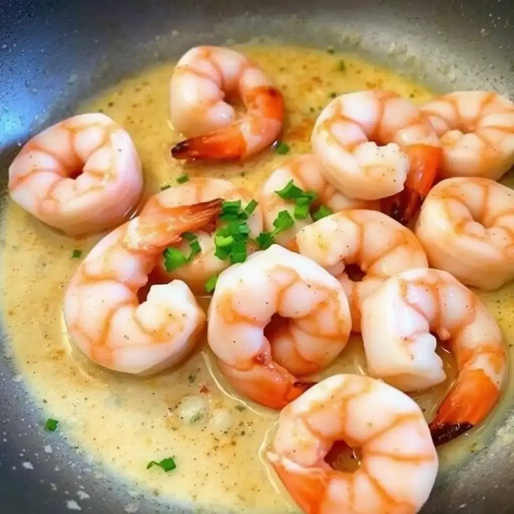 Shrimp sautéing in a pan with a light spicy cream sauce, topped with fresh parsley.